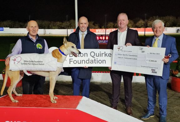 Image shows 4 men and a greyhound - the men are Chris Walsh with his retired Greyhound Gold, Tim Lucey CEO of Greyhound Racing Ireland, Dan Quirke of the Dillon Quirke Foundation, and Pat Flanagan Chairman of Rásaíocht Con Éireann, pictured with a large cheque to highlight the €12,000  raised for the Dillon Quirke Foundation